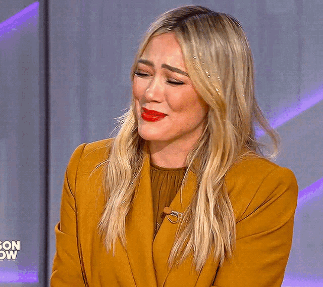 a woman wearing a yellow jacket and red lipstick is crying on a television show