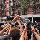 a crowd of people are holding up their phones to take a picture of a woman standing on top of a car .