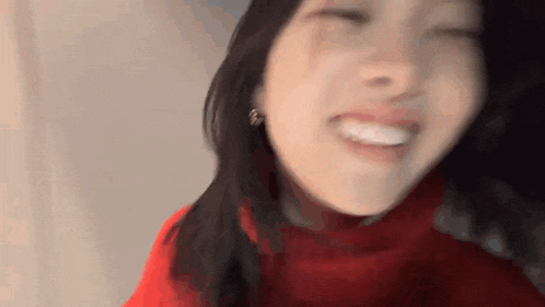 a close up of a woman wearing a red sweater and earrings smiling with her eyes closed .