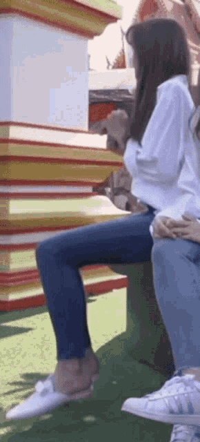 a woman in a white shirt and blue jeans sits on a bench
