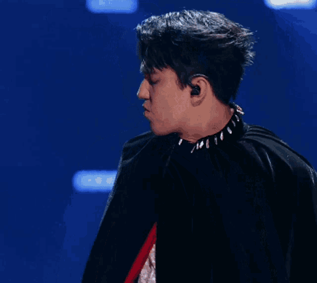 a young man wearing a black cape and a choker looks at the camera