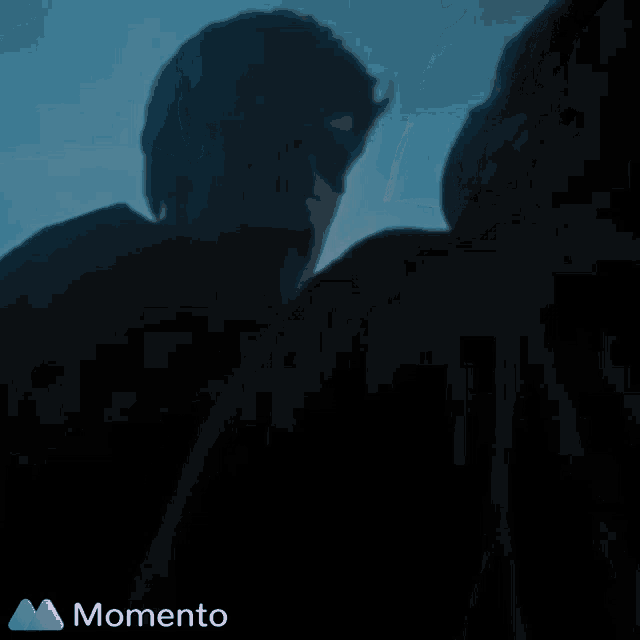a couple of people standing next to each other in the dark with a momento logo on the bottom right