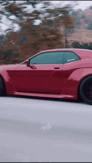 a red car is driving down a road with trees in the background