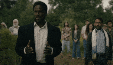 a man in a suit and white shirt stands in front of a group of people