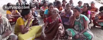 a group of people are sitting in a circle on the ground talking to each other .
