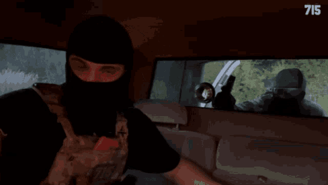 a man in a mask is sitting in a car with the number 715 on the bottom left