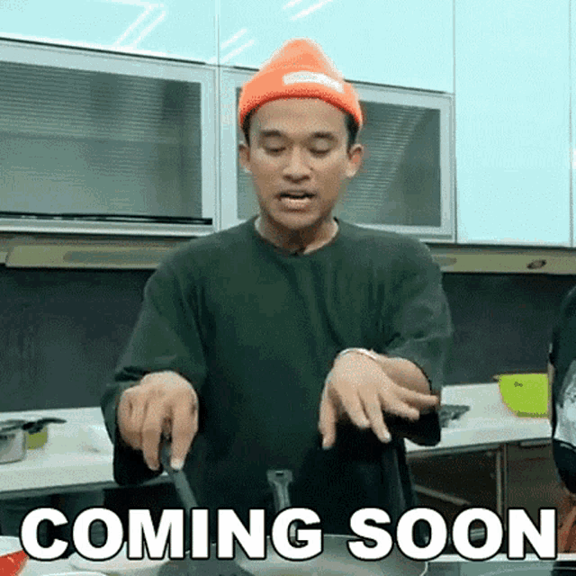 a man in an orange hat is holding a knife in a kitchen with the words coming soon above him .