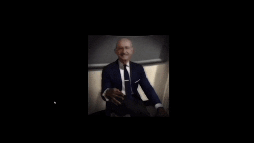 a blurry picture of a man in a suit and tie sitting in a chair .