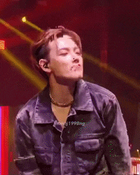 a young man wearing a denim jacket is standing on a stage with his hands on his chest .