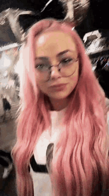 a woman with pink hair and glasses is standing in front of a crowd at a carnival .