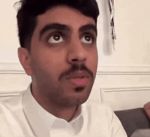a man with a mustache is wearing a white shirt and looking up .