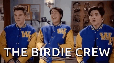 three boys wearing varsity jackets are standing next to each other in a room and laughing .