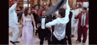 a group of people are dancing in a room with a woman in a pink dress and a man in a tuxedo .