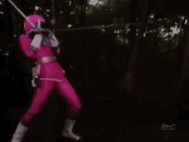 a woman in a pink costume is standing in the woods with a gun .
