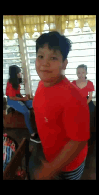 a boy in a red shirt is standing in a room with other people