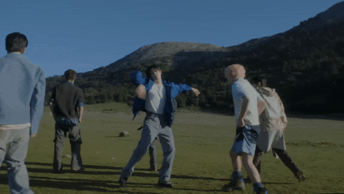 a group of people are standing in a grassy field with mountains in the background