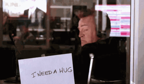 a man sitting in front of a computer with a sign that says i need a hug