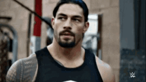 a man with a beard is wearing a black tank top and looking at the camera .