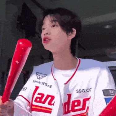 a young man in a baseball uniform is holding a red bat and a red balloon .