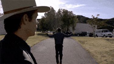 a man in a cowboy hat walking down a road with his arms outstretched