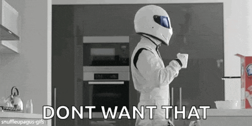 a man in a racing suit is holding a cup of coffee in a kitchen .