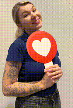 a woman in a blue shirt is holding a red sign with a white heart on it