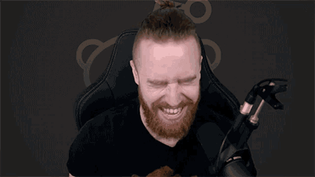 a man with a beard is sitting in a chair in front of a microphone and laughing .