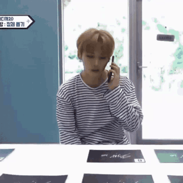 a young man in a striped shirt is talking on a cell phone .