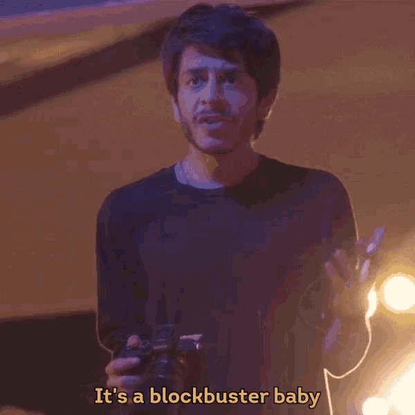 a man holding a camera with the words it 's a blockbuster baby above him
