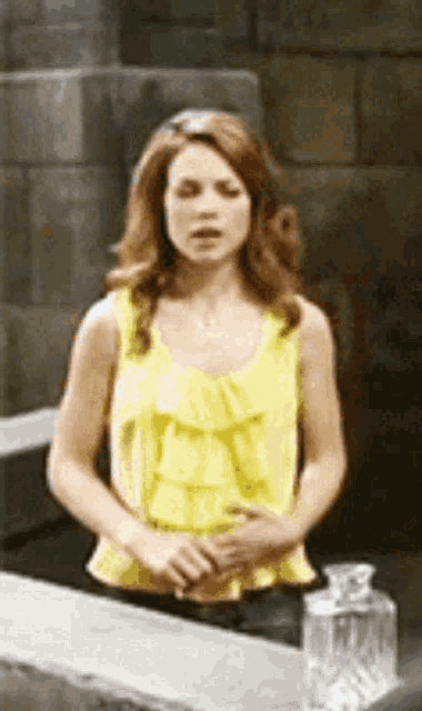 a woman in a yellow tank top is standing in front of a bottle of alcohol .