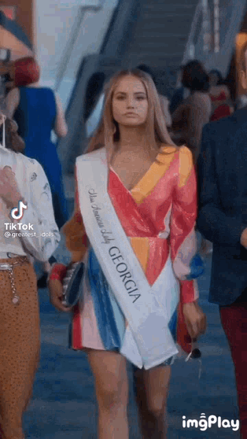 a woman wearing a sash that says georgia is walking down a street .