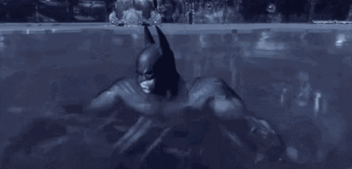 a man in a batman costume is flying through the air in a smokey room .