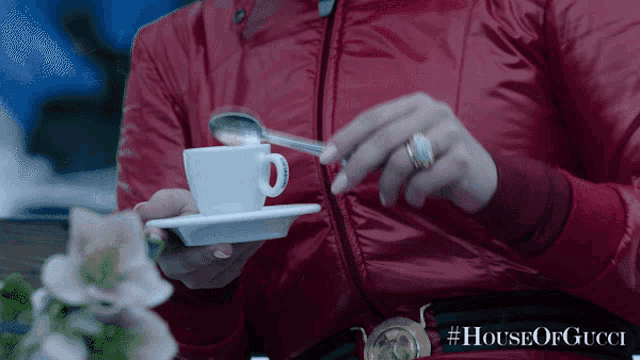 a woman in a red jacket is holding a cup of coffee and a saucer