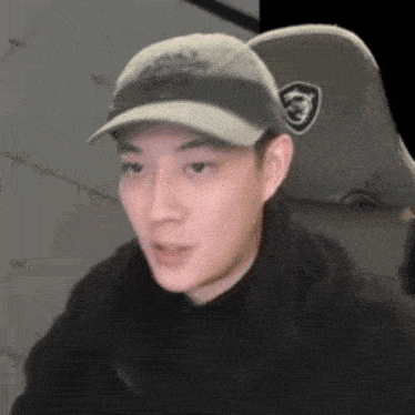 a man wearing a baseball cap and a black jacket is sitting in a chair .