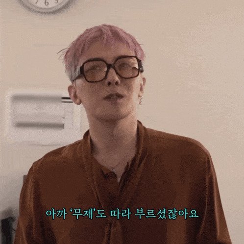 a man with pink hair wearing glasses and a brown shirt with foreign writing on it