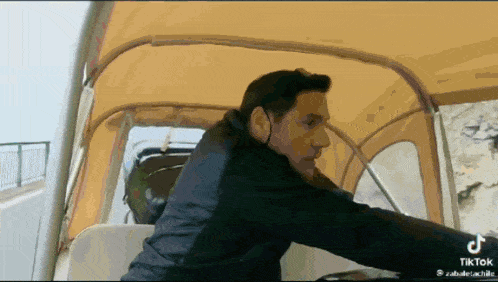 a man in a black jacket is driving a boat with a yellow roof