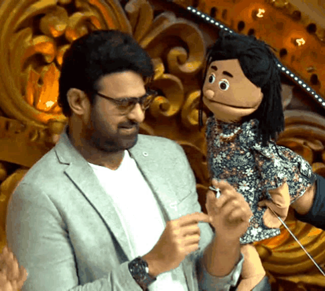 a man in a suit and glasses holds a puppet in his hands