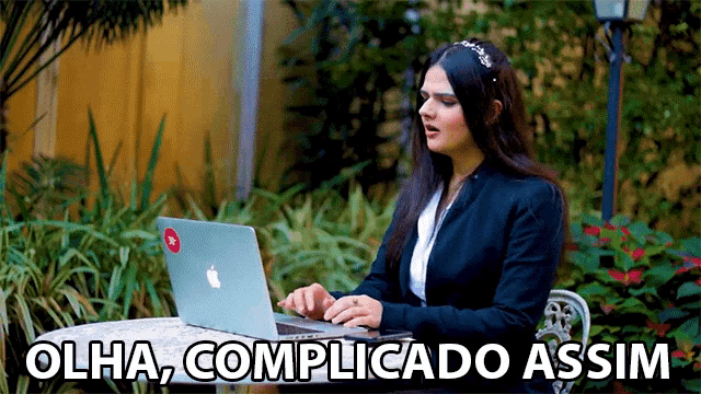 a woman sitting at a table with a laptop and the words olha complicatado assim written above her
