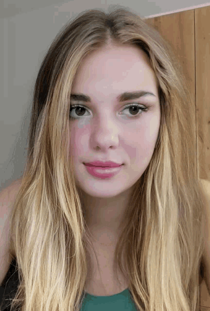 a woman with long blonde hair and a green shirt looks at the camera