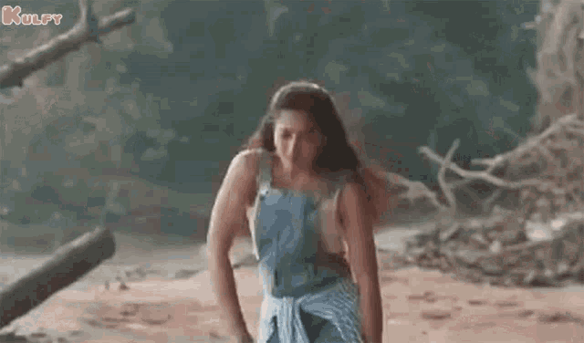 a woman in overalls is standing on a beach with her hands on her hips .