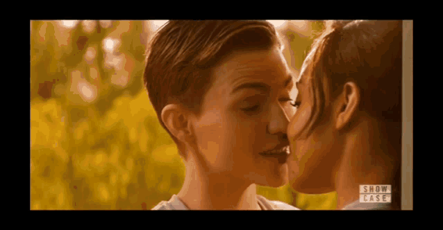 a couple of women are kissing each other in front of a tree .