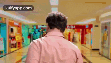 a man in a pink shirt is walking down a mall hallway .