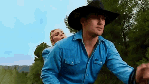 a man in a cowboy hat is holding a woman on his back