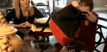 a woman and a boy are sitting at a table holding a red bag