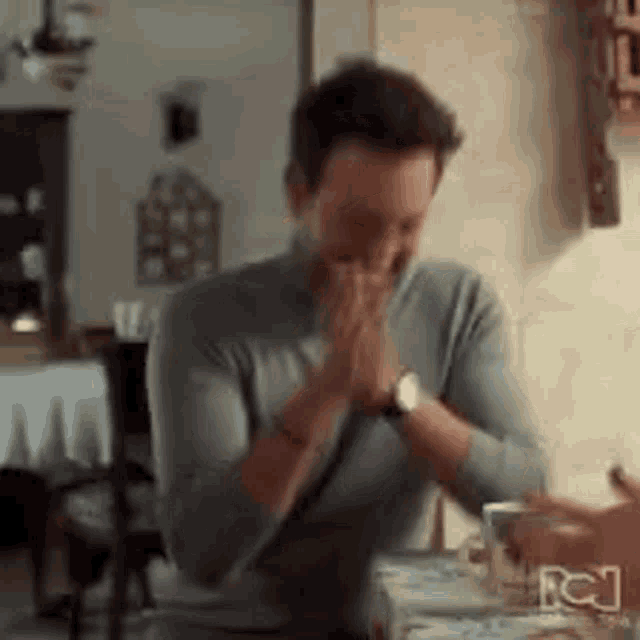 a man is sitting at a table with his hands folded in prayer in a kitchen .