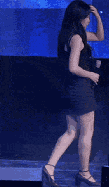 a woman in a black dress is dancing on a stage with a blue background