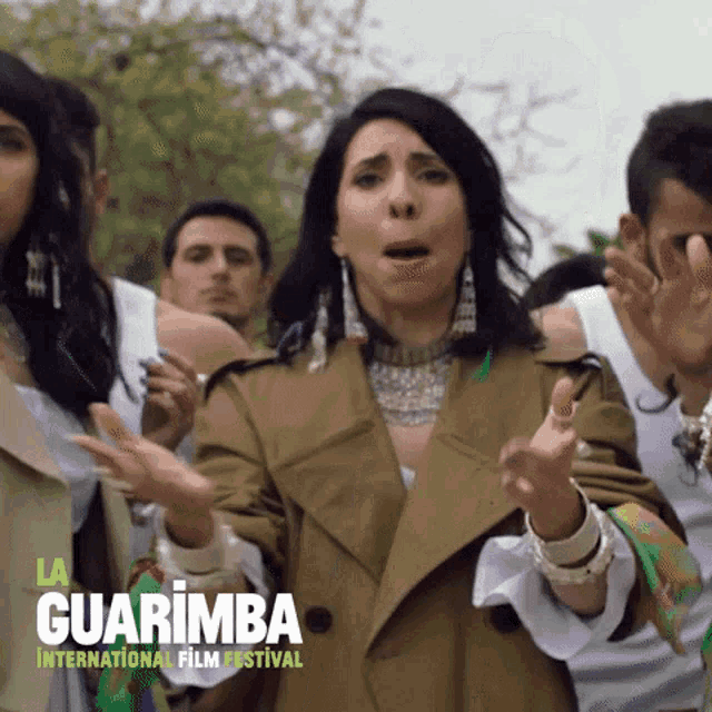 a woman in a trench coat stands in front of a group of people at the guarimba international film festival