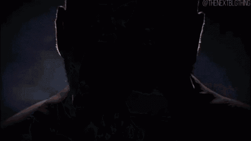 a muscular man without a shirt is standing in a dark room with his hands on his hips .