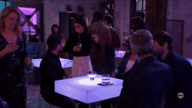 a group of people are gathered around a table with a purple light