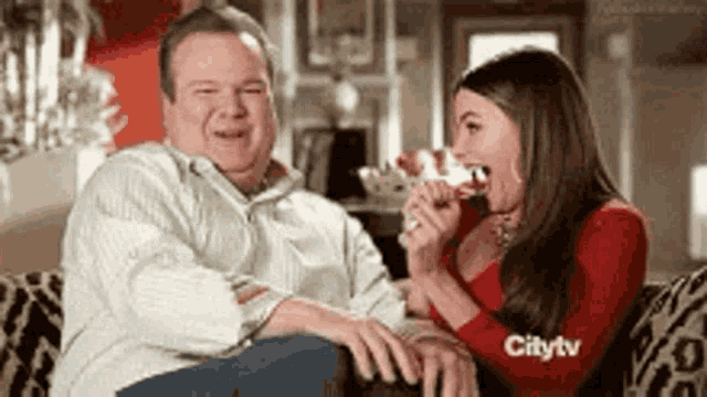 a man and a woman are sitting on a couch and the woman is eating a piece of cake .